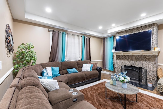 living room featuring a tray ceiling, a stone fireplace, and hardwood / wood-style flooring