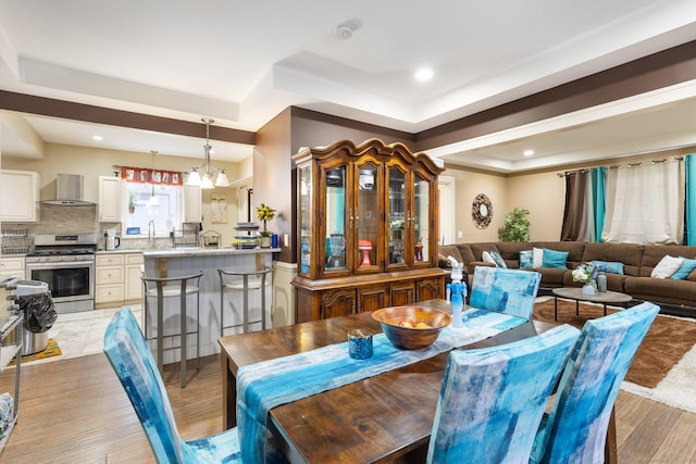 dining room featuring a chandelier, a raised ceiling, sink, and light hardwood / wood-style flooring