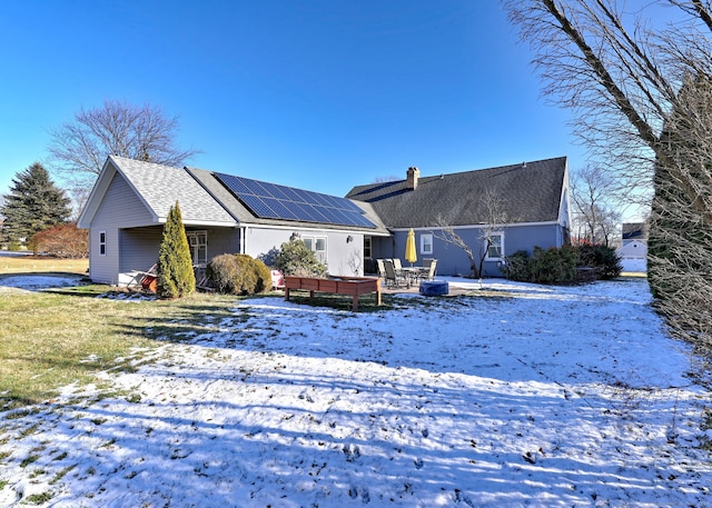 snow covered house featuring solar panels and a patio