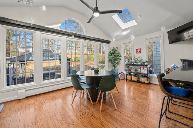 dining area featuring vaulted ceiling with skylight, ceiling fan with notable chandelier, light wood-type flooring, and baseboard heating