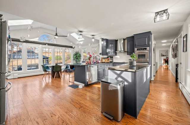 kitchen with ceiling fan, wall chimney range hood, light hardwood / wood-style floors, lofted ceiling, and appliances with stainless steel finishes