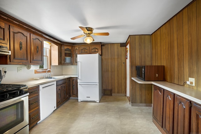 kitchen featuring ceiling fan, wood walls, white appliances, and sink