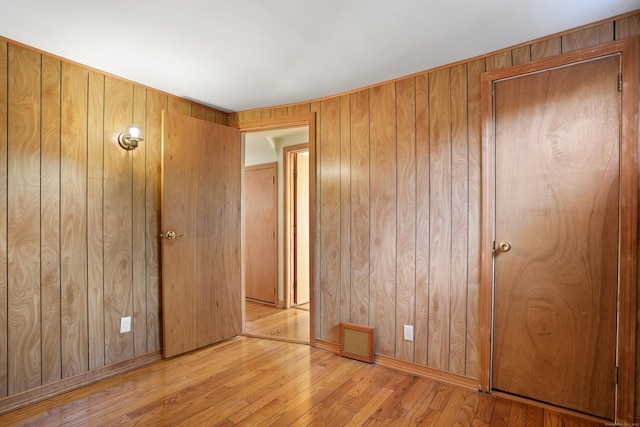 unfurnished bedroom featuring light wood-type flooring, wooden walls, and a closet