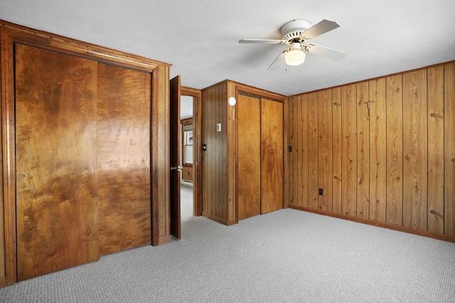 unfurnished bedroom featuring ceiling fan, wooden walls, and light colored carpet