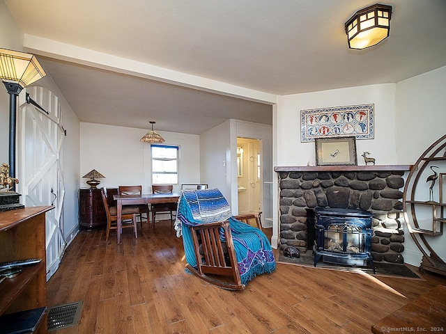 living room with beamed ceiling, a wood stove, and hardwood / wood-style floors