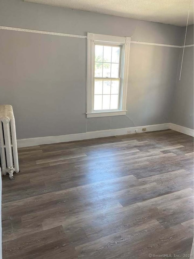 spare room featuring dark hardwood / wood-style flooring, radiator heating unit, and a textured ceiling