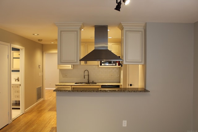 kitchen featuring kitchen peninsula, decorative backsplash, island range hood, sink, and light hardwood / wood-style floors