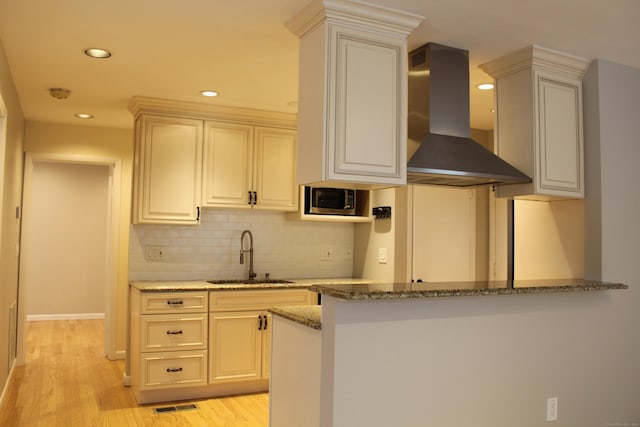 kitchen featuring wall chimney range hood, light hardwood / wood-style flooring, stone counters, and sink