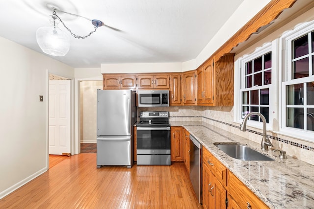 kitchen with backsplash, sink, light wood-type flooring, appliances with stainless steel finishes, and light stone countertops