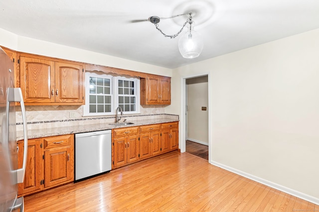 kitchen featuring tasteful backsplash, light wood-type flooring, stainless steel dishwasher, light stone counters, and sink