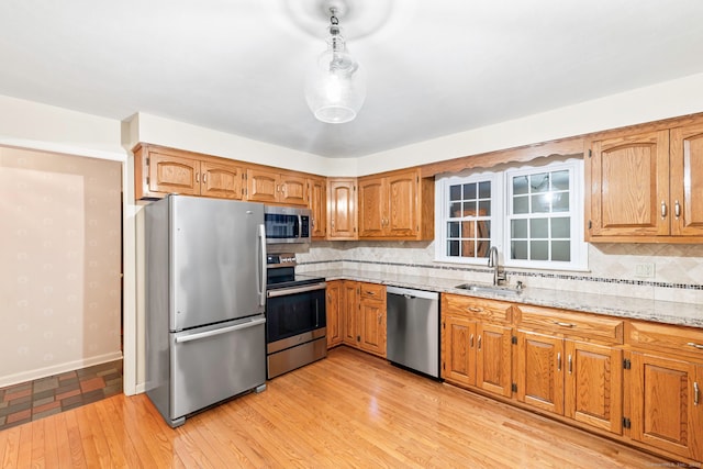 kitchen with stainless steel appliances, backsplash, light stone countertops, light hardwood / wood-style flooring, and sink