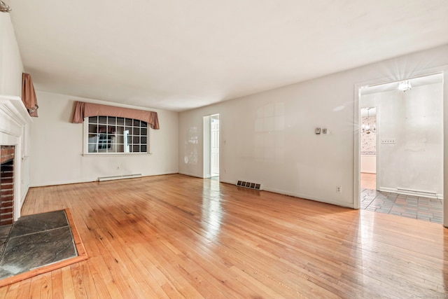 unfurnished living room with a brick fireplace, a baseboard heating unit, and light hardwood / wood-style flooring