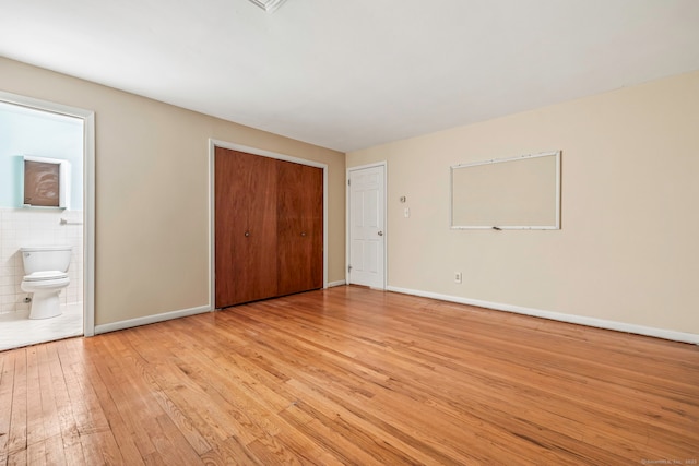 unfurnished bedroom featuring ensuite bathroom, a closet, and light hardwood / wood-style floors