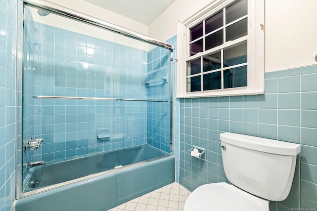 bathroom with toilet, tile walls, and shower / bath combination with glass door