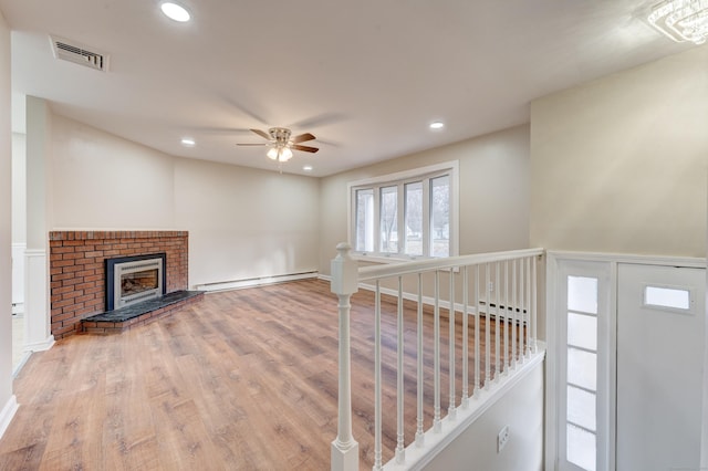 unfurnished living room with a fireplace, hardwood / wood-style flooring, ceiling fan, and a baseboard heating unit