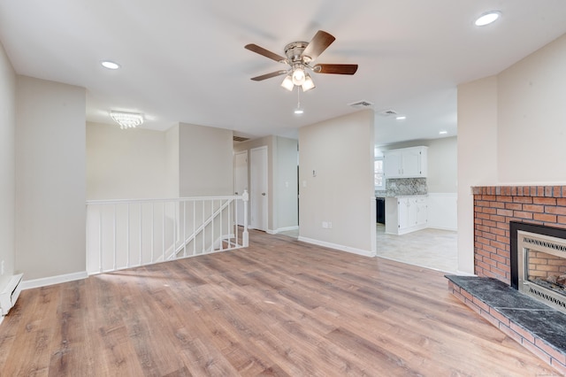 unfurnished living room with ceiling fan, light wood-type flooring, and a brick fireplace