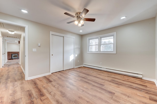 unfurnished bedroom with ceiling fan, a fireplace, light hardwood / wood-style floors, and a baseboard heating unit