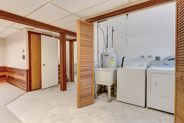 laundry area with sink, electric water heater, washer and clothes dryer, and wood walls