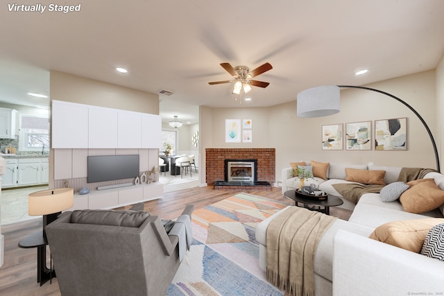 living room with a brick fireplace, ceiling fan, and light hardwood / wood-style flooring