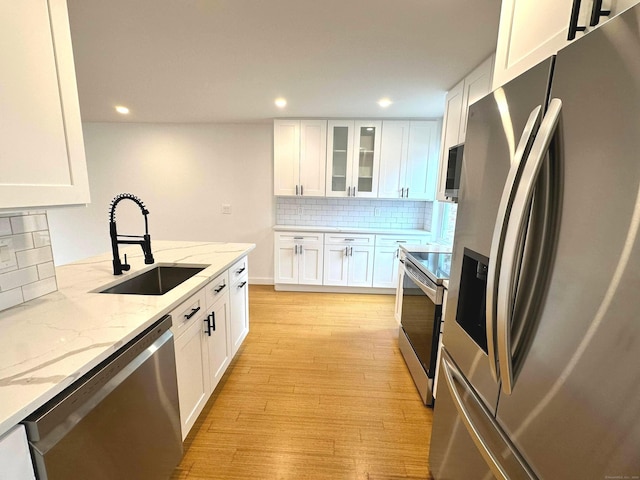 kitchen featuring light stone countertops, decorative backsplash, stainless steel appliances, sink, and white cabinetry