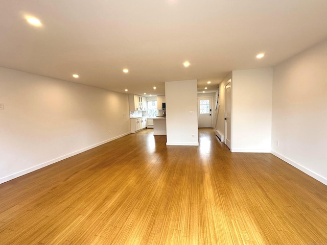 unfurnished living room with baseboard heating and light hardwood / wood-style floors