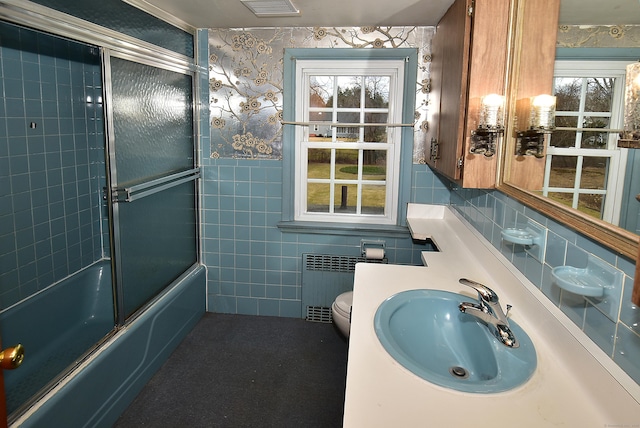 full bathroom featuring radiator, bath / shower combo with glass door, sink, toilet, and tile walls