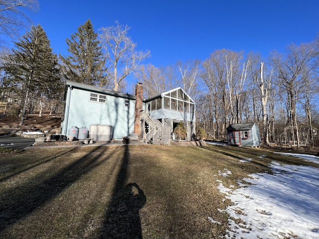 view of front of house with a sunroom, a chimney, a storage shed, and an outdoor structure