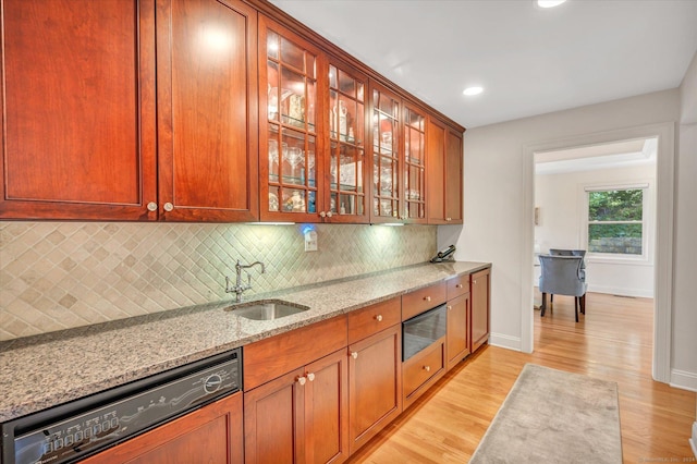 kitchen featuring light stone countertops, backsplash, sink, light hardwood / wood-style flooring, and black dishwasher