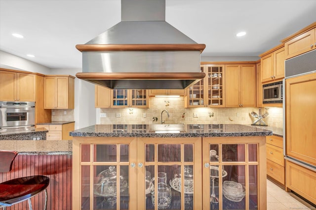 kitchen with backsplash, built in appliances, dark stone countertops, light tile patterned floors, and island range hood