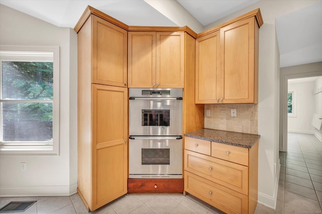 kitchen with double oven, decorative backsplash, light tile patterned floors, and dark stone counters