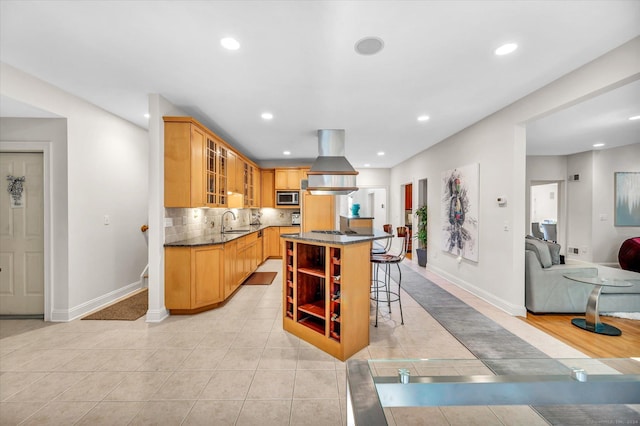 kitchen featuring stainless steel microwave, a kitchen island, light tile patterned floors, island range hood, and a breakfast bar area