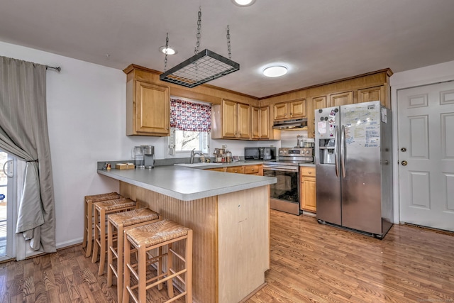 kitchen with sink, light wood-type flooring, appliances with stainless steel finishes, a kitchen bar, and kitchen peninsula