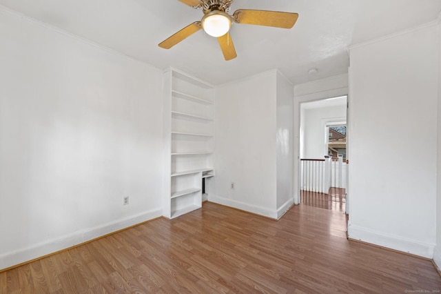 empty room featuring hardwood / wood-style floors, built in features, ceiling fan, and crown molding