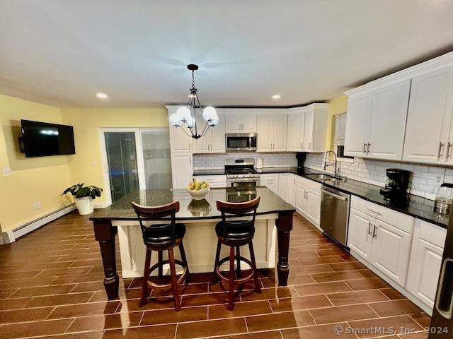 kitchen featuring stainless steel appliances, baseboard heating, sink, a center island, and white cabinetry