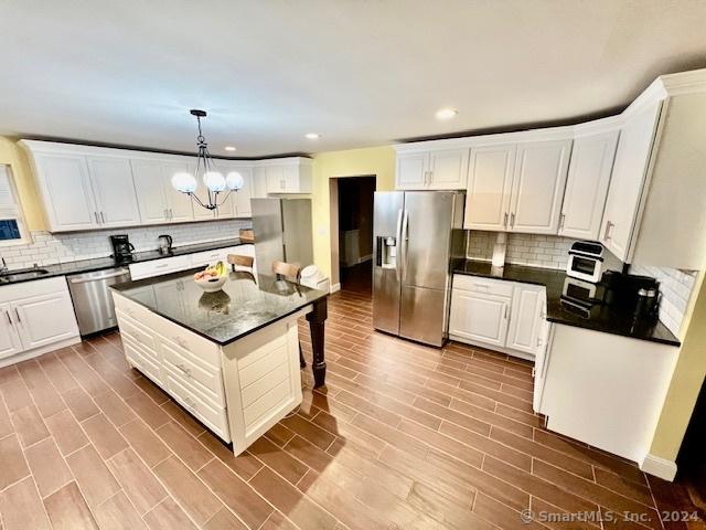 kitchen featuring a center island, stainless steel appliances, hanging light fixtures, white cabinetry, and a chandelier