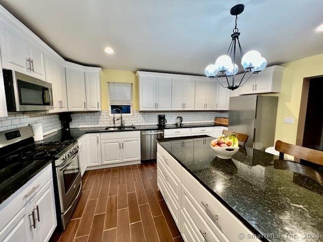 kitchen with pendant lighting, appliances with stainless steel finishes, wood tiled floor, white cabinets, and dark stone countertops