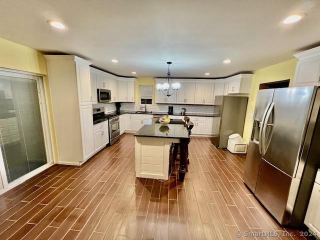 kitchen with dark countertops, a center island, hanging light fixtures, stainless steel appliances, and white cabinetry