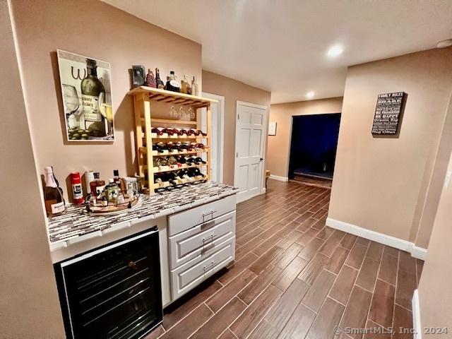 bar with wine cooler, baseboards, wood finish floors, and a bar