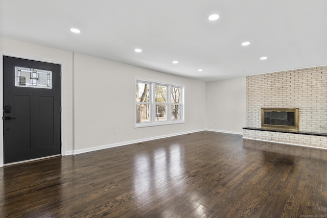 unfurnished living room featuring dark hardwood / wood-style flooring and a brick fireplace