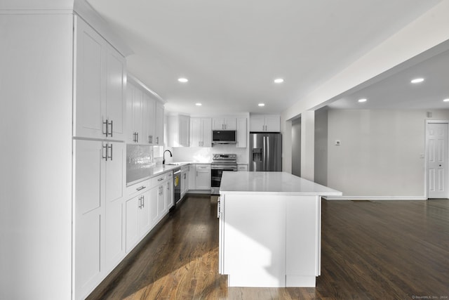 kitchen featuring dark wood-type flooring, appliances with stainless steel finishes, a center island, tasteful backsplash, and white cabinets