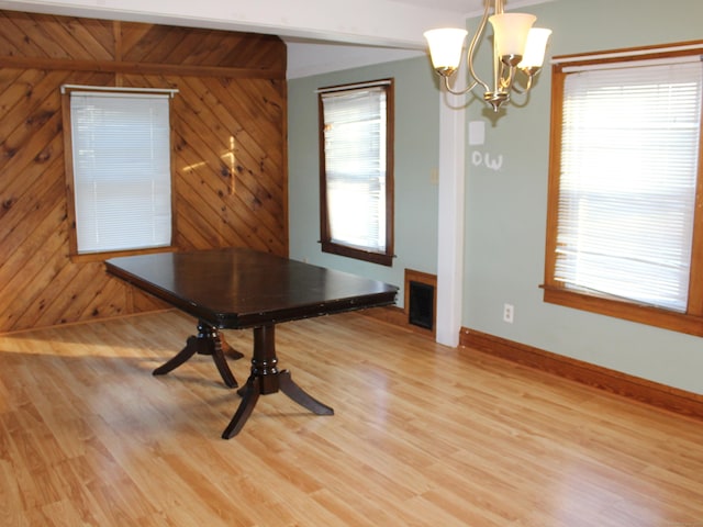 unfurnished dining area featuring wooden walls, light hardwood / wood-style floors, and a notable chandelier