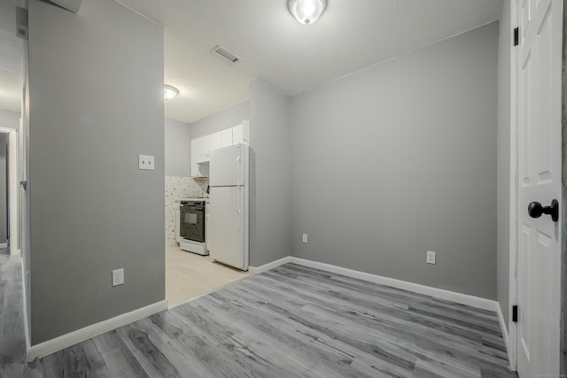 spare room with white cabinetry, light hardwood / wood-style flooring, and a textured ceiling