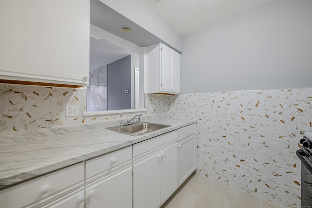 kitchen with stainless steel electric stove, sink, light tile patterned floors, a textured ceiling, and white cabinetry