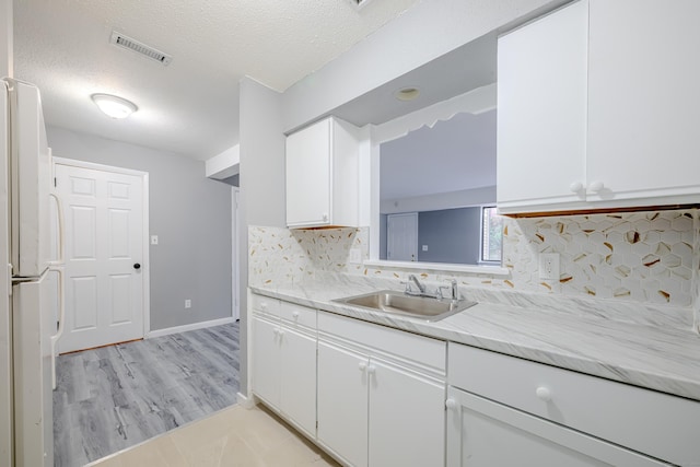 kitchen with sink, a textured ceiling, white fridge, decorative backsplash, and white cabinets