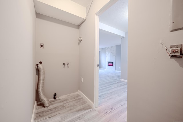 clothes washing area with hookup for a washing machine, hookup for an electric dryer, a textured ceiling, and light hardwood / wood-style floors