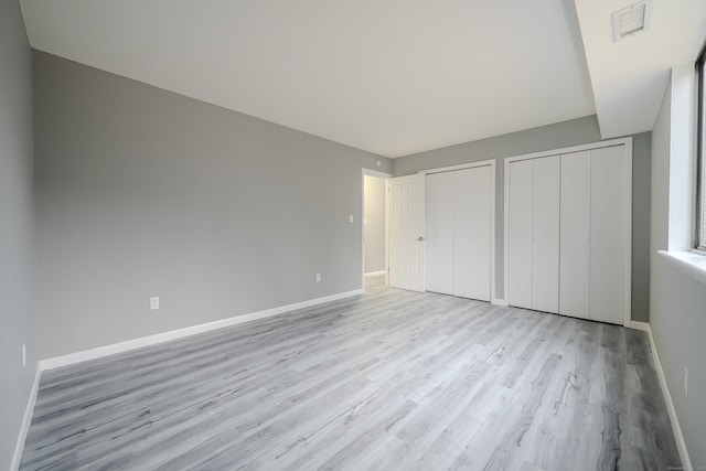 unfurnished bedroom featuring two closets and light hardwood / wood-style floors