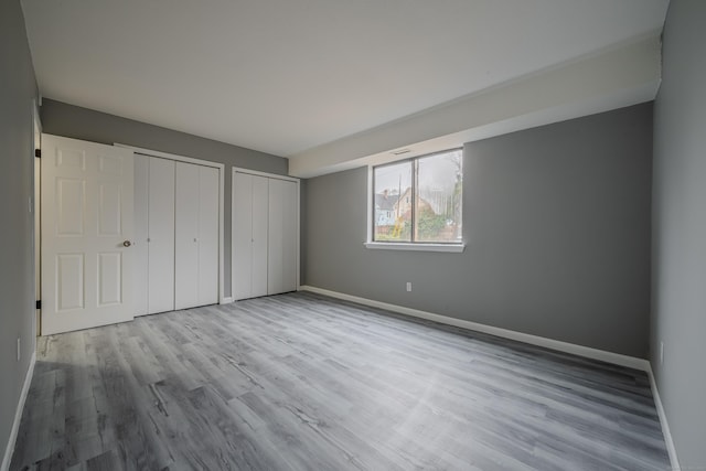 unfurnished bedroom with light hardwood / wood-style floors and multiple closets