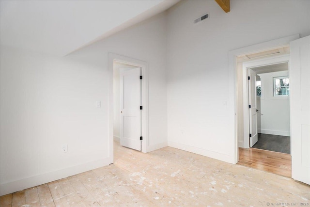 unfurnished room featuring lofted ceiling with beams and light wood-type flooring