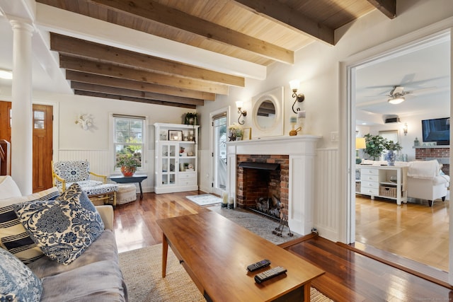 living room with beamed ceiling, ceiling fan, wood ceiling, a brick fireplace, and light wood-type flooring