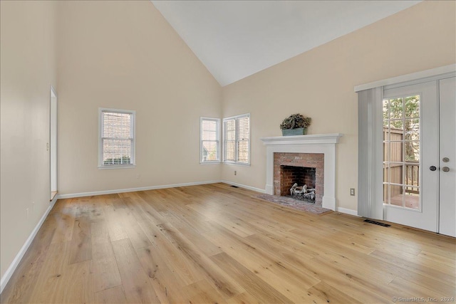 unfurnished living room featuring a brick fireplace, light hardwood / wood-style flooring, high vaulted ceiling, and plenty of natural light